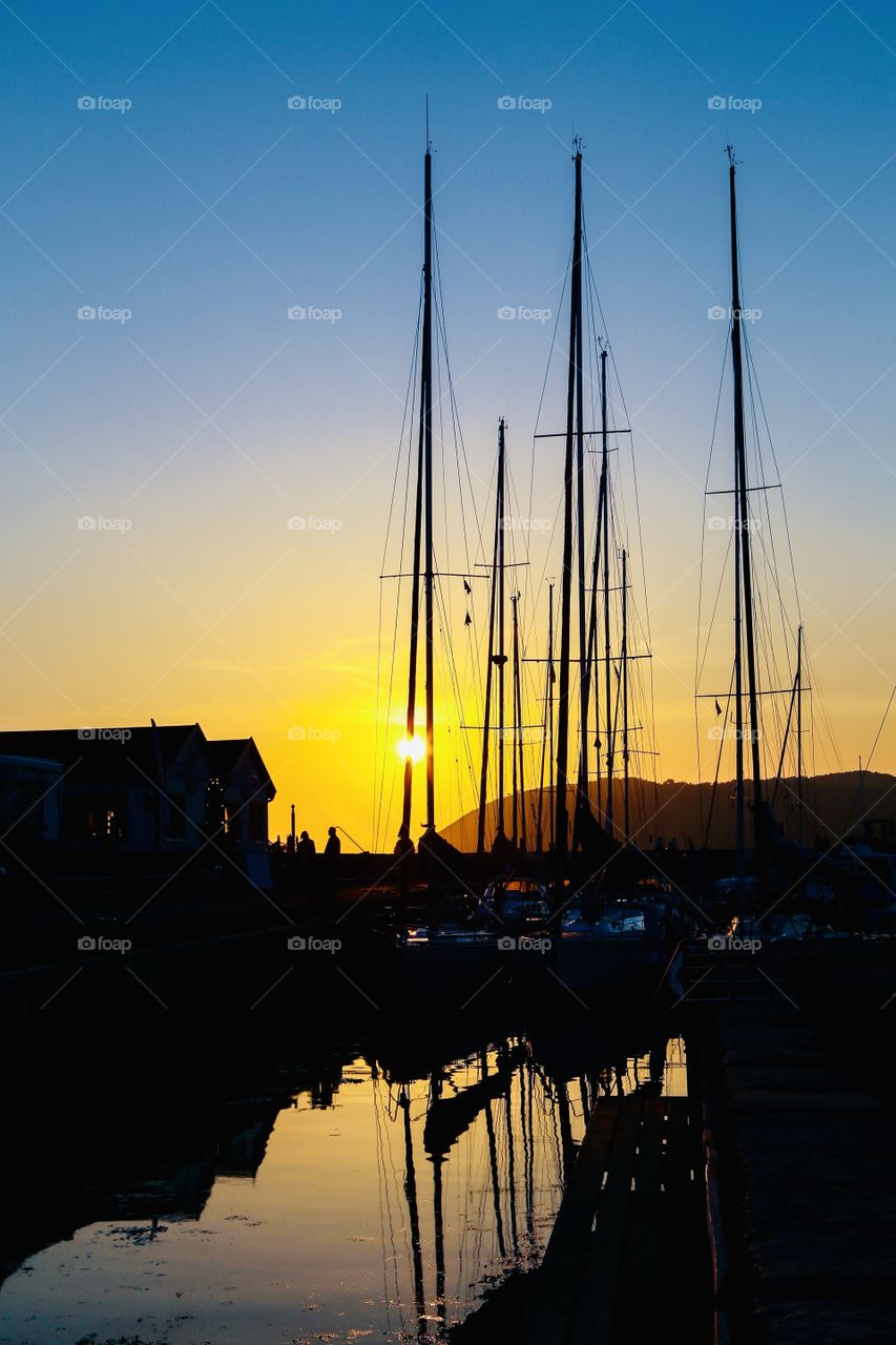 Sailing boats in a harbor with a mountain behind and the sunset coloring the sky