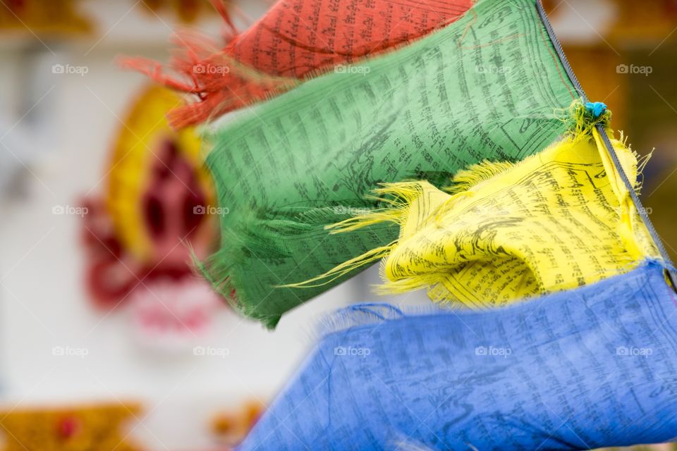 Colorful prayer flags in wind. Colorful prayer flags moving in the wind. Flags have foreign text. Out of focus shrine in the background 