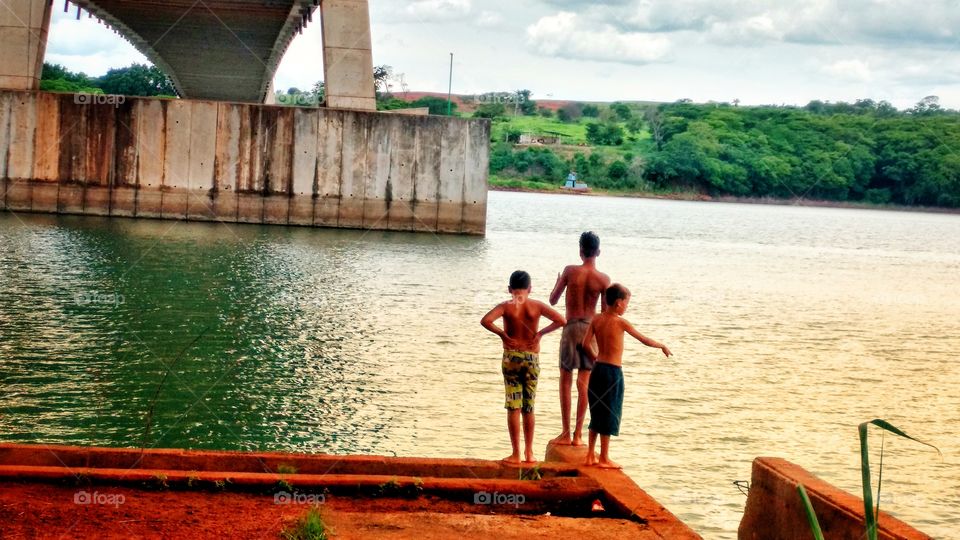 Crianças à beira das aguas. Rio, ponte de concreto.