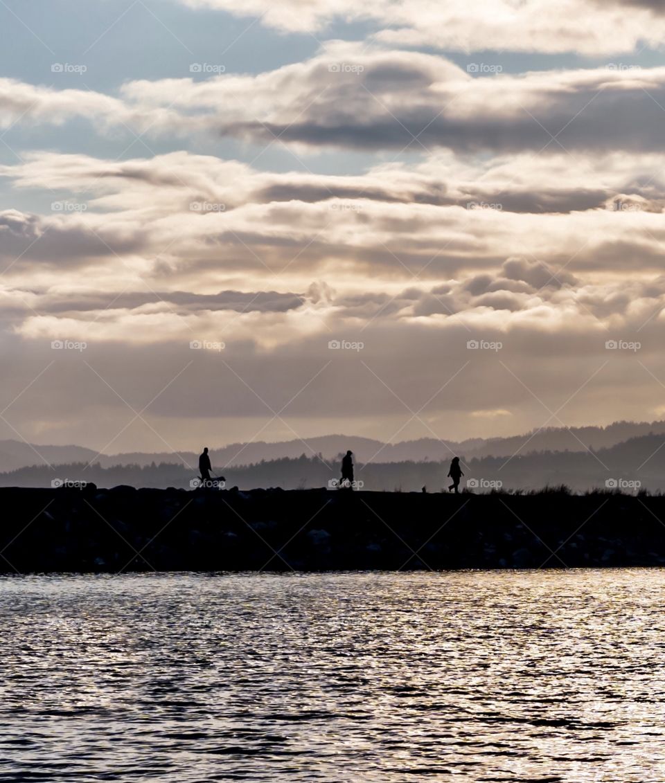 People stroll down walkway into the ocean as the sun sets and darkness descends 