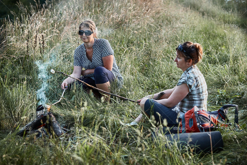 Women roasting a marshmallows over a campfire on meadow. Vacations close to nature. Candid people, real moments, authentic situations