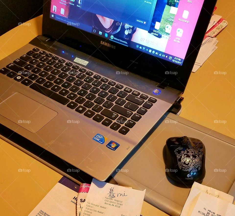 Desk area ready for working from home. Home office necessities include laptop, mouse, mouse pad & paperwork. Table works as work area for business.