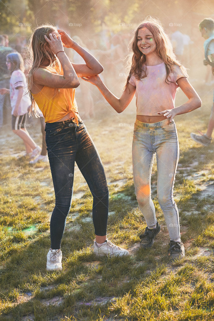 Portrait of happy smiling young girls with colorful paints on faces and clothes. Two friends spending time on holi color festival. Real people, authentic situations