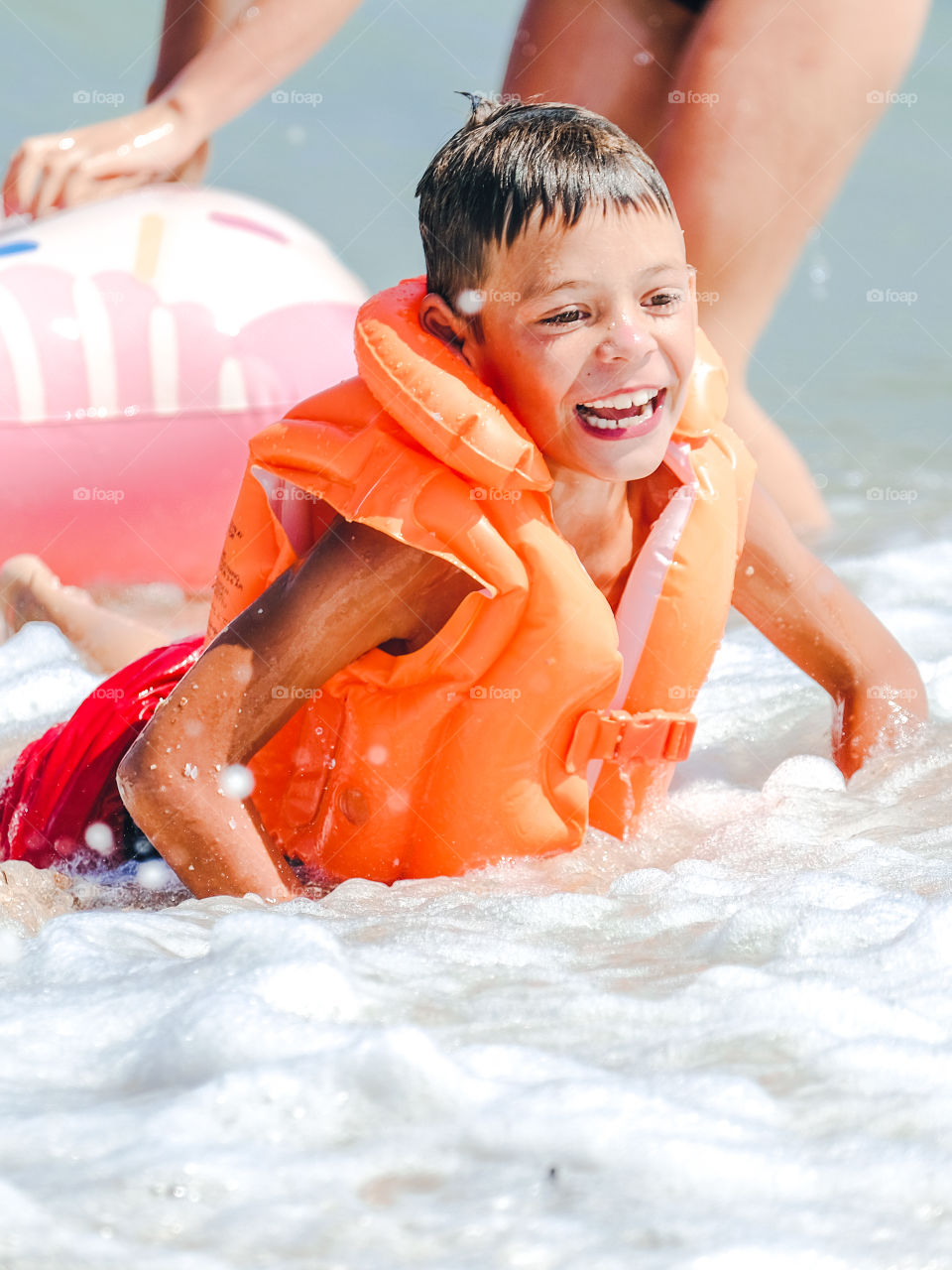 Smiling boy in orange inflatable vest swimming in the sea