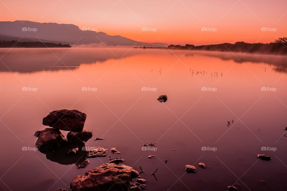 sunrise over a lake with rocks in foreground