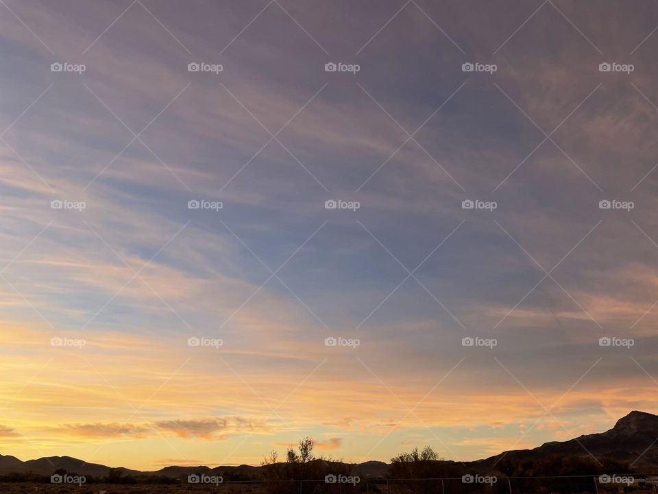 A cloudy sunset with yellow tinted clouds and mountains. 