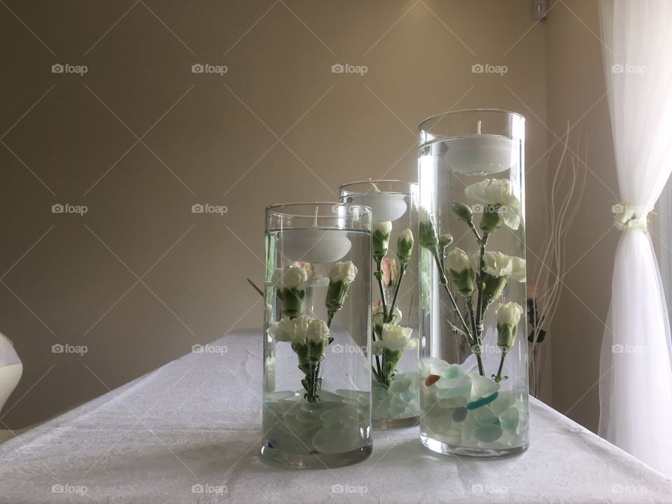 Beautiful White flowers and a candle in glass vase filed with water for a wedding.