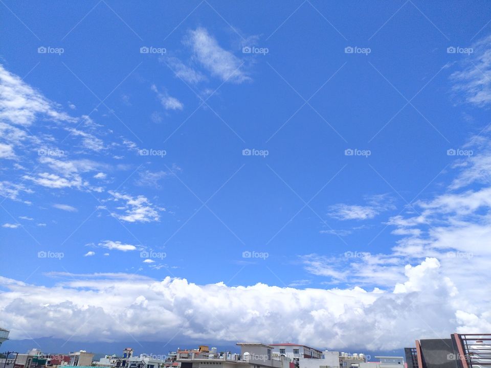 Flakes of white clouds floating across a beautiful blue sky over Mussoorie hills