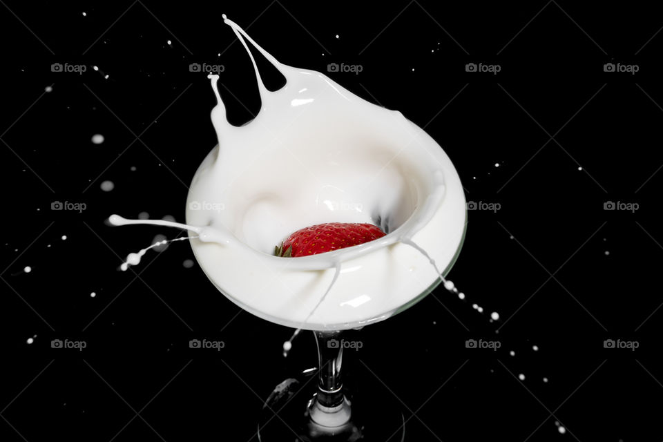 Fresh strawberry falling into glass of milk