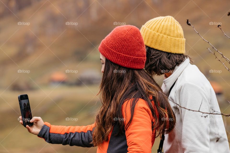 Two young women friends, using phone to take selfies for social media accounts, while doing a hike in nature.