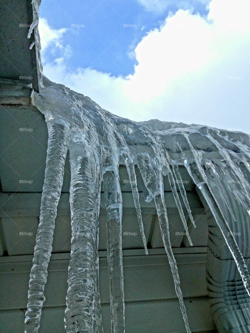 Winter is coming, rain in gutters, then frozen over with icicles hanging from roof. Blue sky with clouds, then snow coming. It's a freezing cold day!