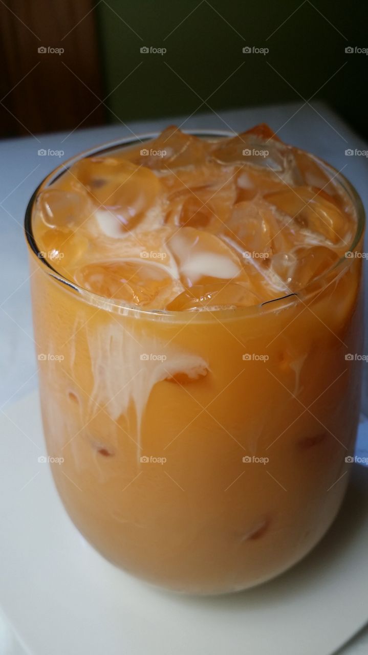 A glass of sweet Thai Iced Tea topped with creamy milk