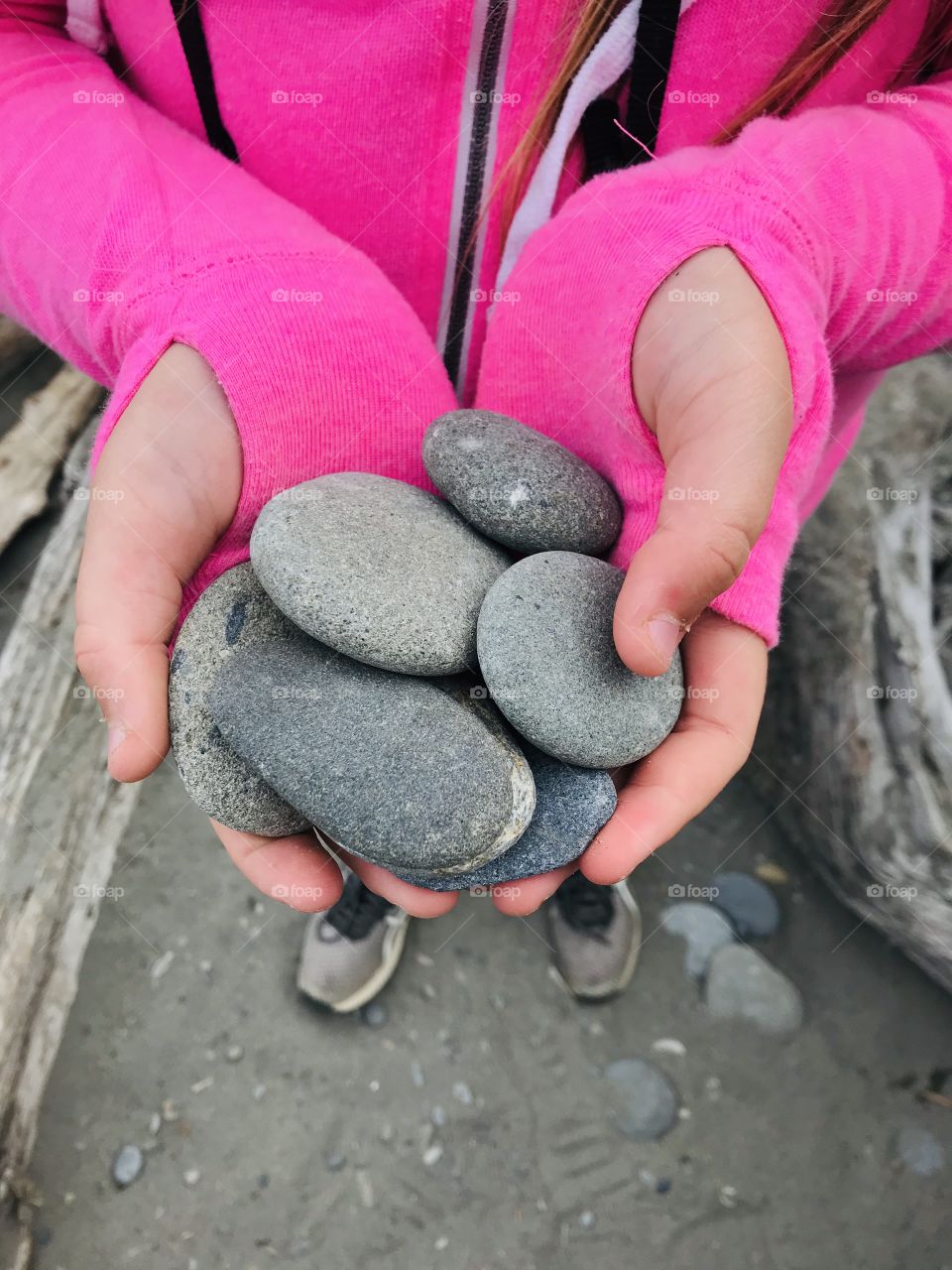 Smooth gray rocks in hands of girl wearing beautiful bright pink sweatshirt and perfect tennis for beach combing! 