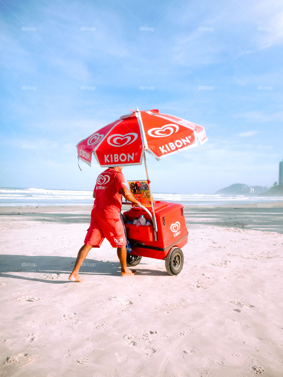 Kibon Ice cream man, at Guarujá, Brasil, in all red clothes and cart. At the seaside, in a beach.
Sorveteiro da Kibon, de vermelho, na praia da Enseada, no Guarujá, à beira mar.