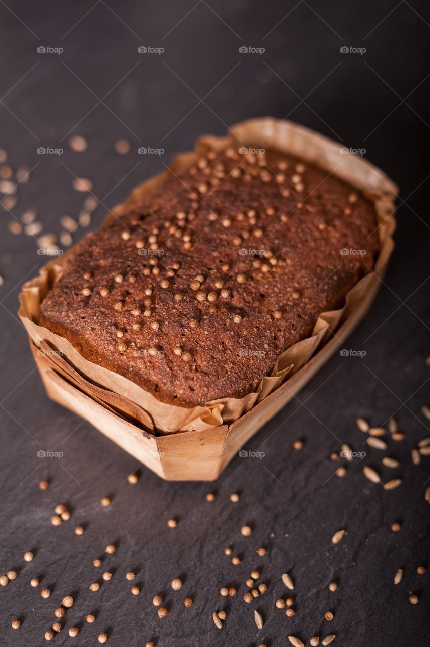 Freshly home baked, wholegrain, rye, brown loaf of bread in wooden baking tray on kitchen work top.