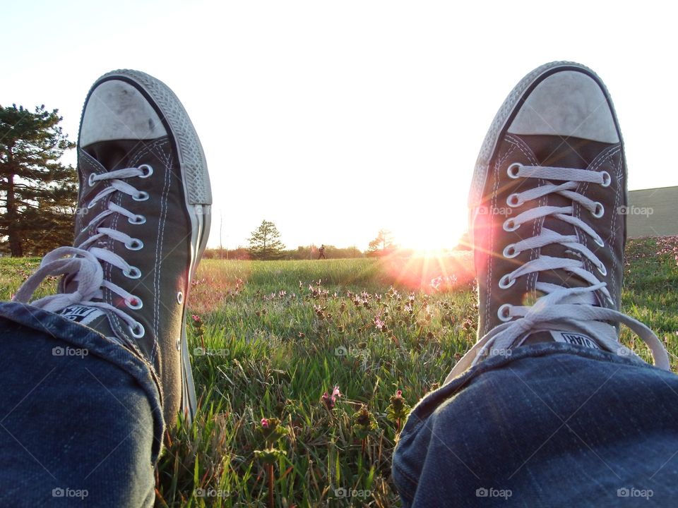 Sitting in the grass 2. Pov perspective view between my shoes looking across a grassy field as the sun goes down at golden hour. 
