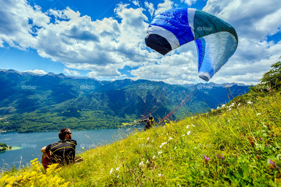 Man sitting on mountain against cloudy sky