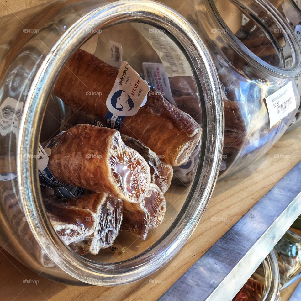 Rawhide dog bones on display in a glass bowl on a shelf in a pet store. Other items are visible further behind in the picture.