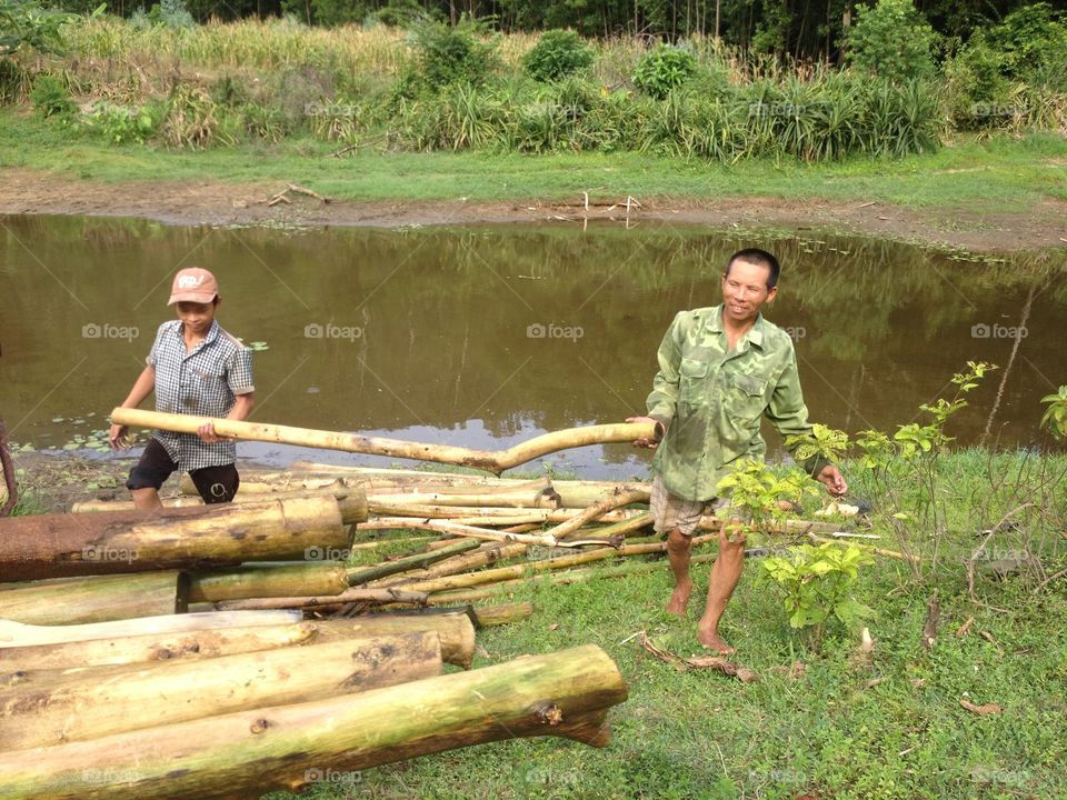 Two man carrying log near river