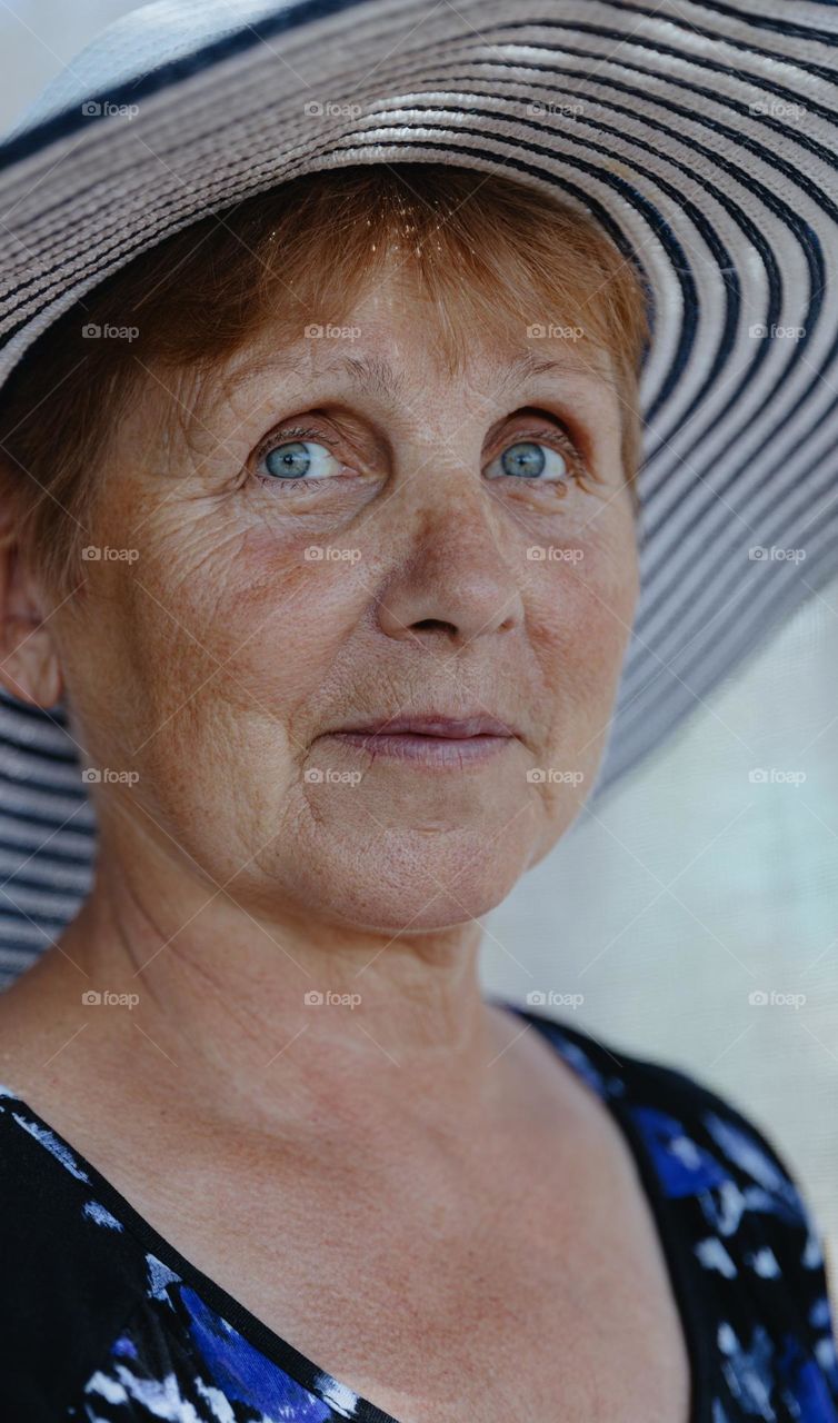 Portrait of one beautiful Caucasian elderly woman with blue-gray eyes in a hat with a smile looks away on a summer day, side view close-