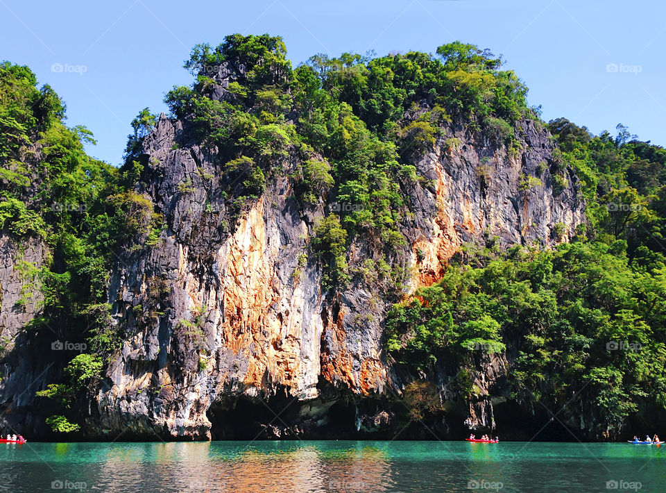 Tiny humans kayaking in blue sea water under the huge Rocky Mountains in Thailand 