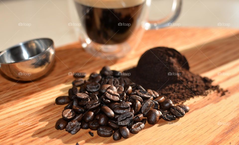 Coffee beans, rounded scoop of ground coffee beans, espresso shot with crema and other implements in early morning light