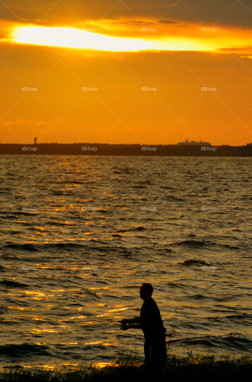 A fisherman fishing on the bay is surrounded by the magnificent sunset! 