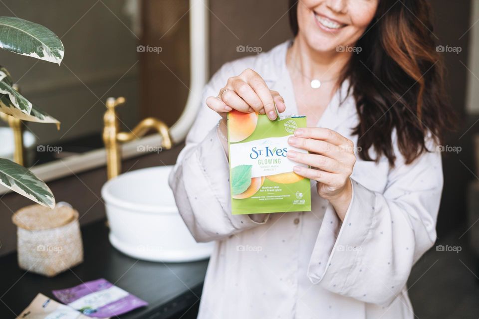 Adult woman with sheet mask in hands in bathroom at home 