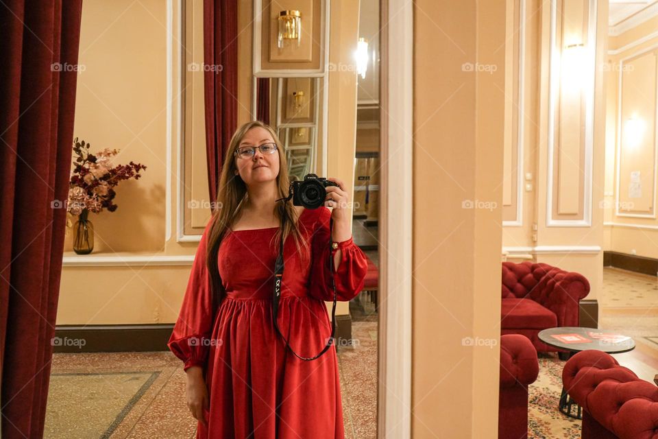 Woman in red dress with professional camera selfie in a mirror 