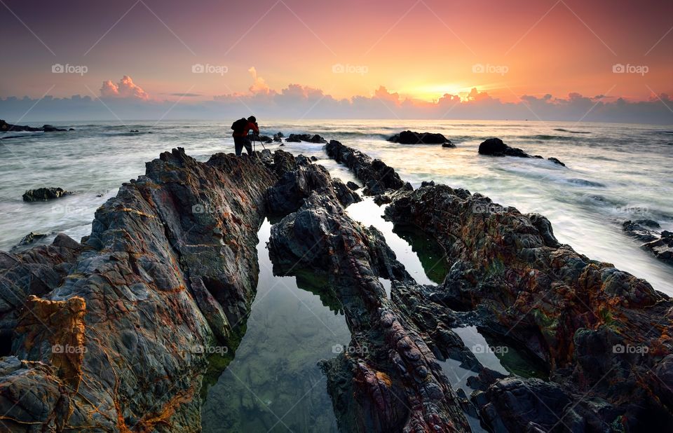 Photographer taking photo during beautiful sunrise at rocky beach