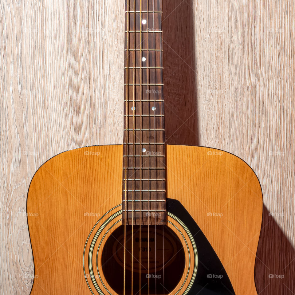 A brown classic acoustic guitar lies on a light wooden background.