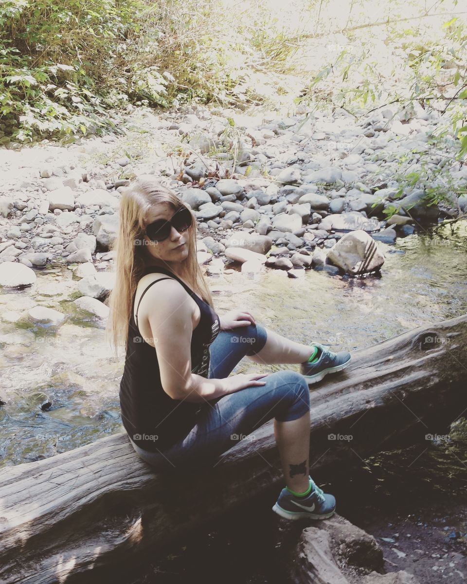 Young woman sitting on wooden log in stream