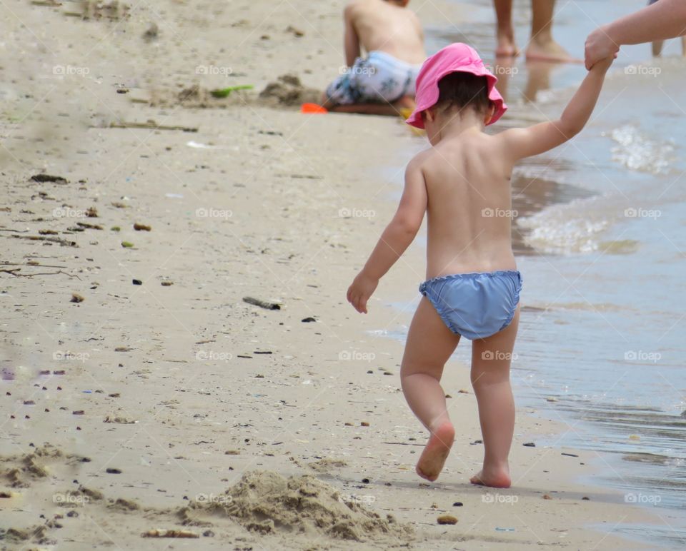 baby triyng first steps with mom in the seashore