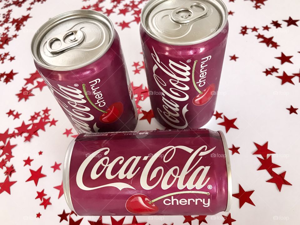 Three cans of Cherry Coca-Cola on a white background with red stars