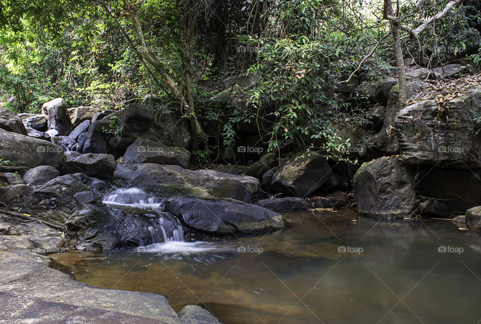 The water flowing over rocks and trees down a waterfall at Khao Ito waterfall , Prachin Buri in Thailand.