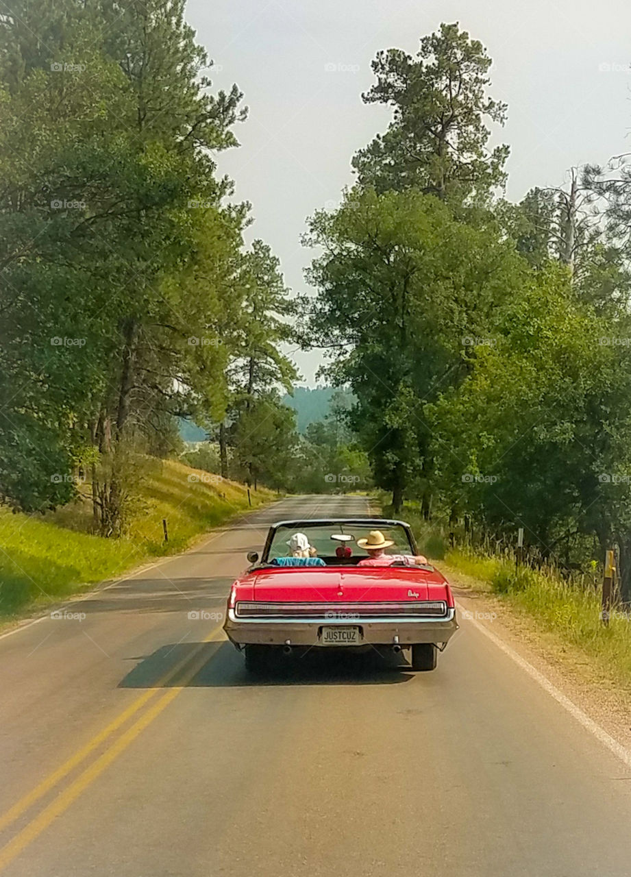 old fashioned red convertible driving along road surfing summer with a man and woman in hats.