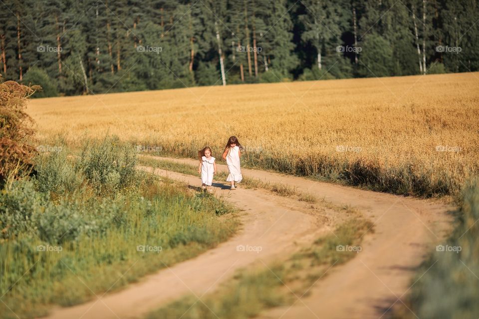 Little sisters running on the sand road through the rye field 