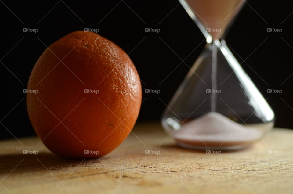 An orange sits on a cutting board next to an hourglass.