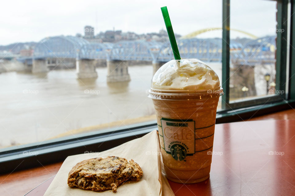 Starbucks frappachino cup and cookie on a table at a Barnes and Noble cafe with a view of a river, bridge and city in the background