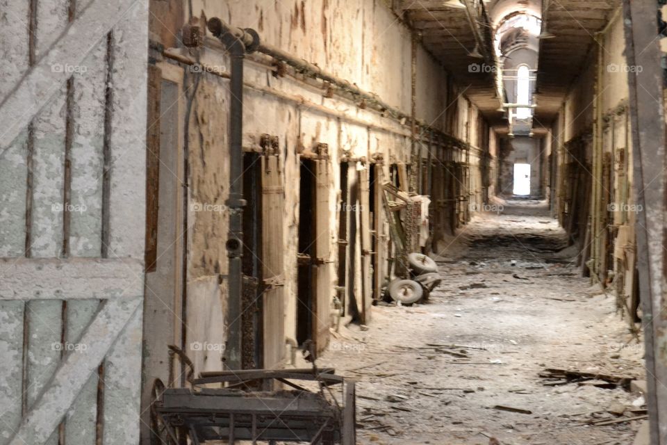 A row of jail cells with broken doors and debris all around in an abandoned prison with dirty floors