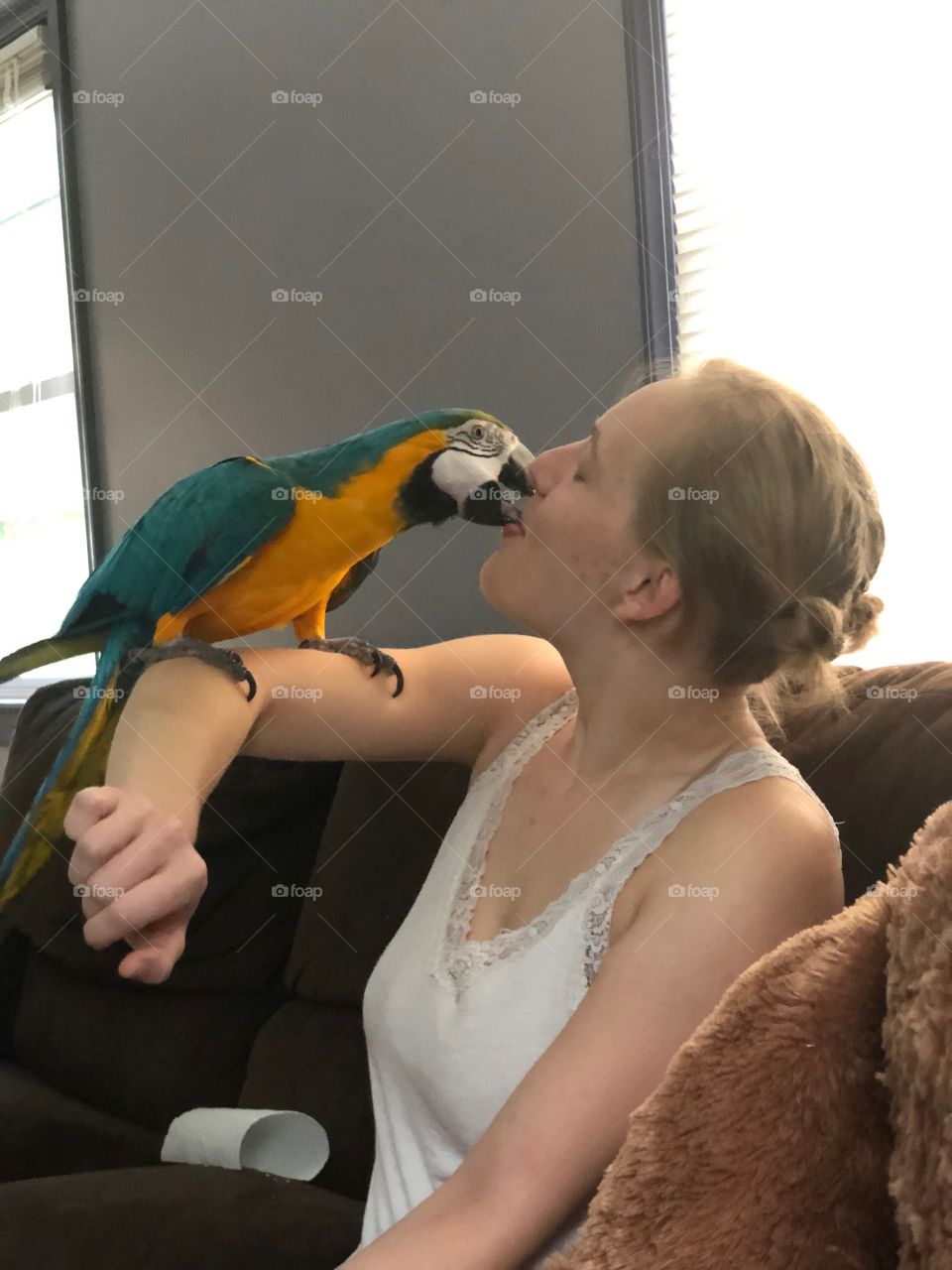 A young woman kisses a darling blue and gold macaw as she rests on her forearm