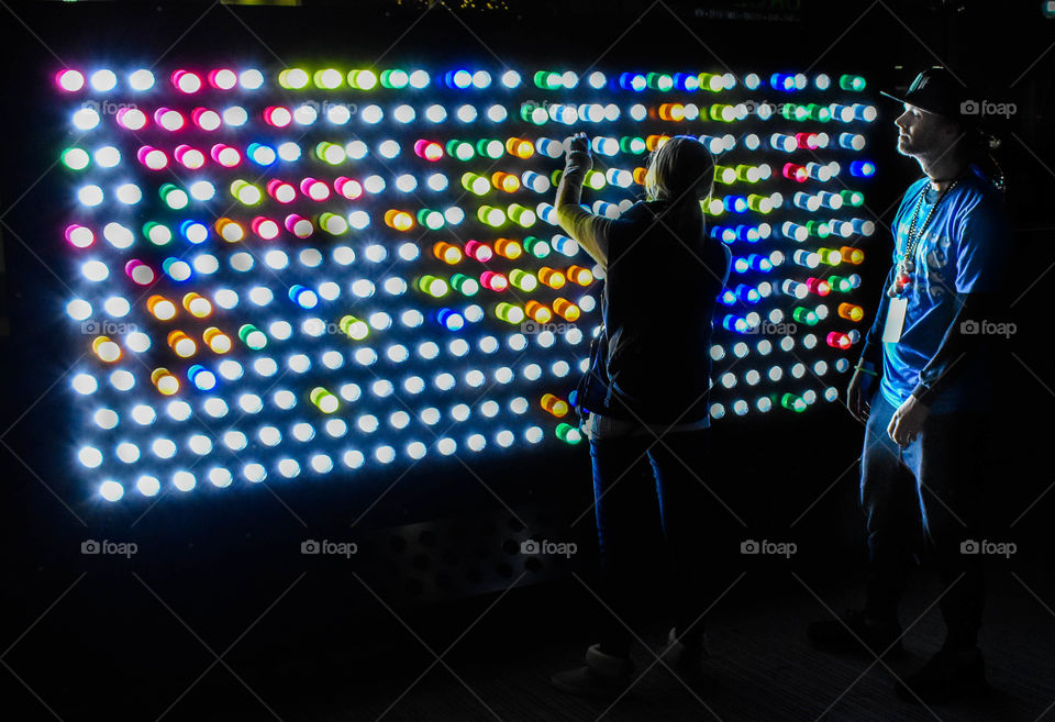 A couple navigates a giant light puzzle full of color and reflection during a wonderful festival. 