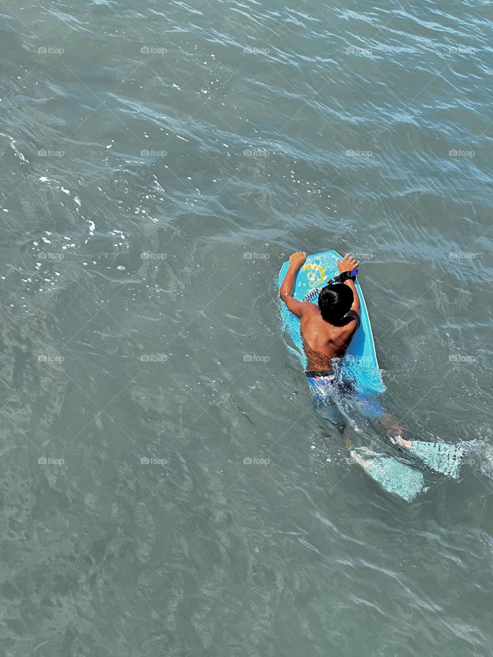 Boy with aqua swim fins on aqua body board looking for the next wave 