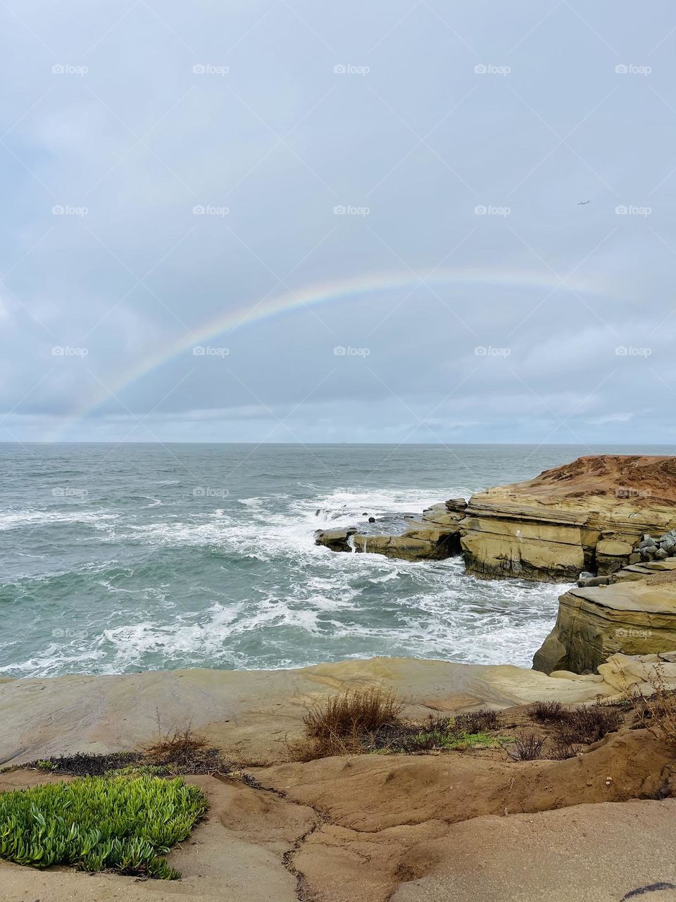 Rainbow over a choppy sea framed by layered rocks
