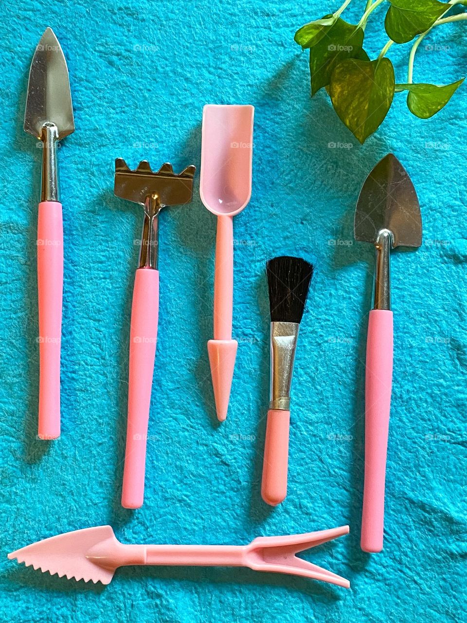 Mini gardening tools in pink against sky blue background with new cutting green leaves.