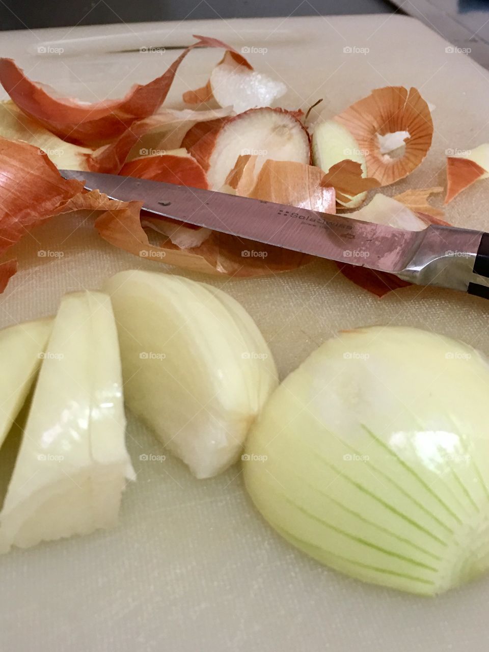 Single peeled onion on cutting board, in process of being sliced, peelings and knife in background 