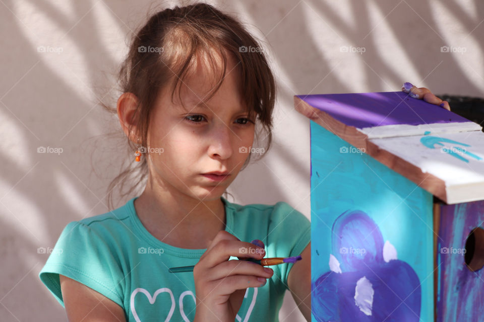 Child painting a wooden bird house