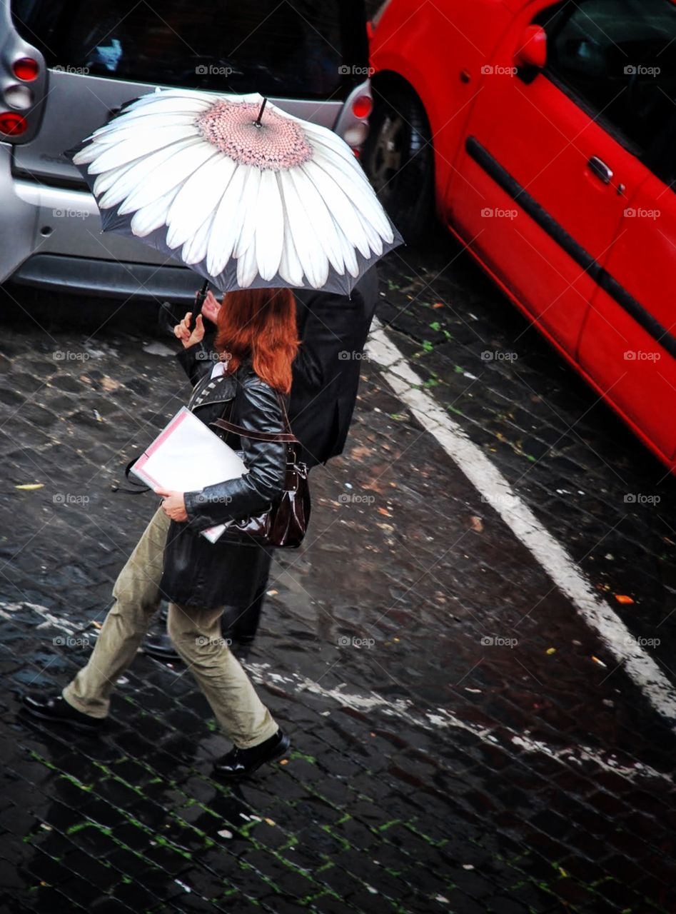 Rainy day daisy . A daisy embellished umbrella shields a red headed woman on a rainy cobblestone street in Rome