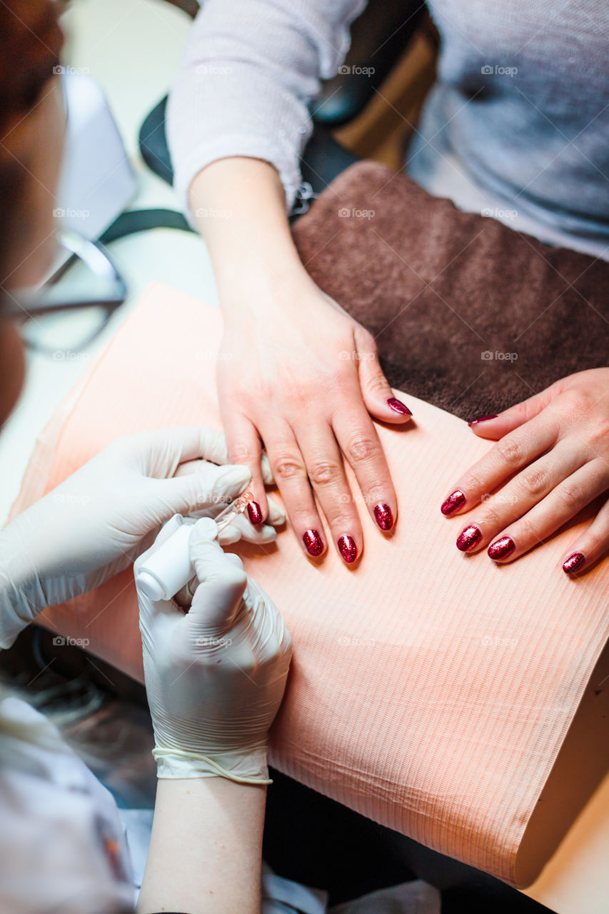 Beautician in a beauty salon doing a hybrid manicure. Painting and styling nails. Woman getting professional nails treatment. Close up of hands