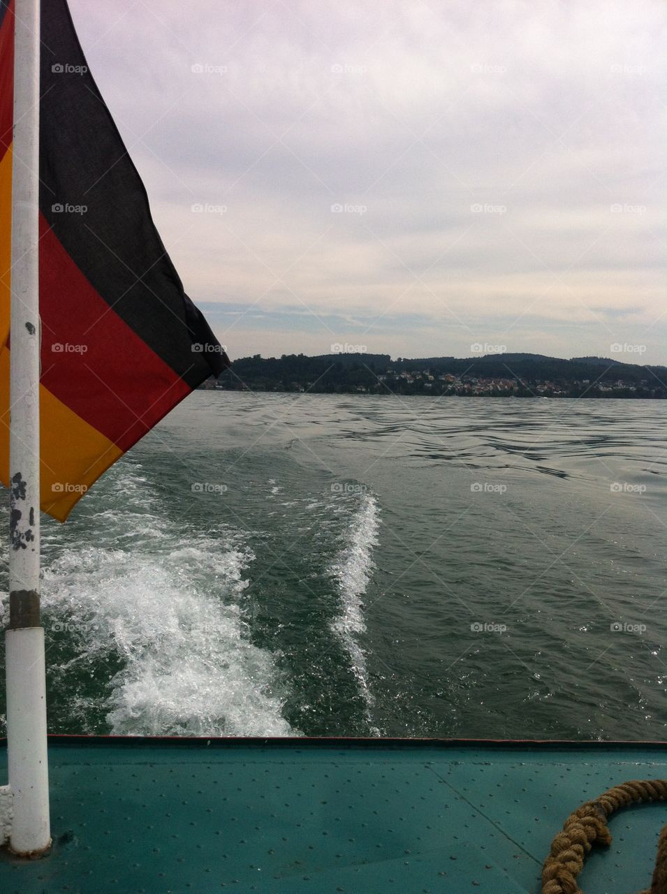 A German flag hanging off the back of a river boat. Cruising on the lake on a beautiful day